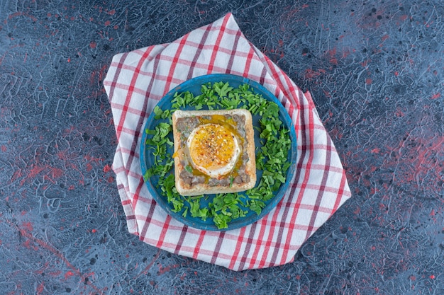 Ein blaues Holzbrett Toast mit Ei und Kräutern.