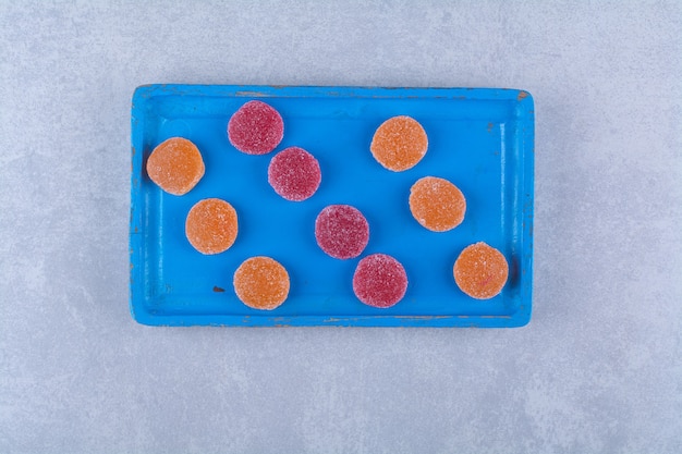 Ein blaues Holzbrett voller roter und oranger Zuckermarmeladen. Foto in hoher Qualität