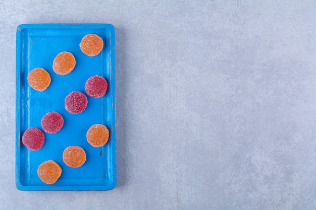 Ein blaues Holzbrett voller roter und oranger Zuckermarmeladen.