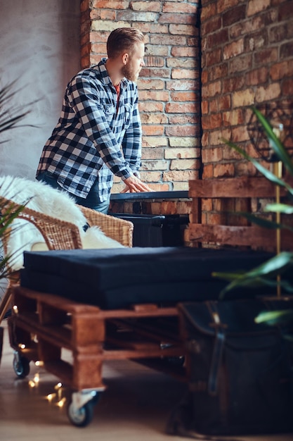 Ein blonder bärtiger Hipster-Mann in Jeans und Fleece-Shirt, der in einem Raum mit Loft-Interieur posiert.