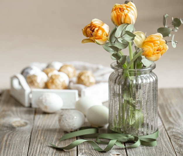 Ein Blumenstrauß in einer Glasvase mit dekorativen Elementen auf einem unscharfen Hintergrund. Osterferienkonzept.
