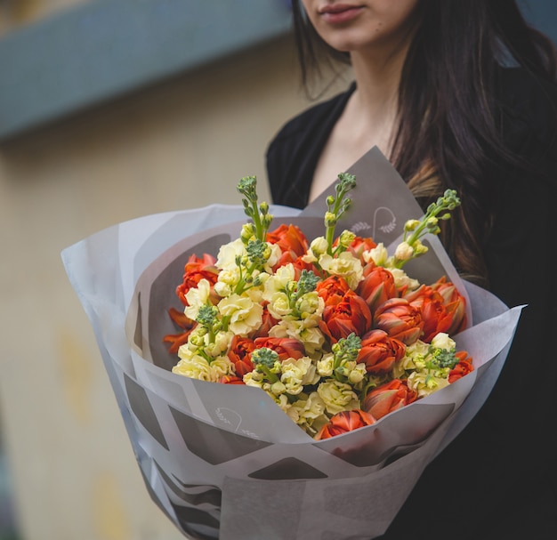 Ein Blumenstrauß von roten Tulpen gelbe Pfingstrosen, die von einer Frau im Schwarzen halten