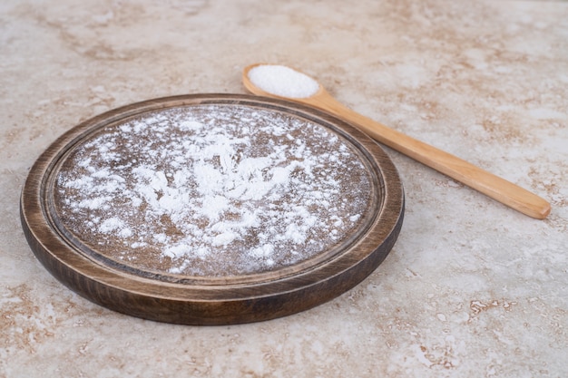 Ein brauner Teller Mehl und ein Holzlöffel Zucker