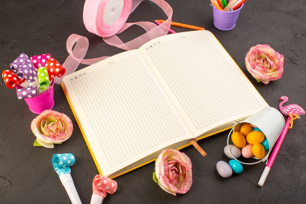 Ein Copybook und Blumen der Draufsicht zusammen mit Bonbons und Dekorationen auf der dunklen Schreibtischbonbon-Farbfotoblume