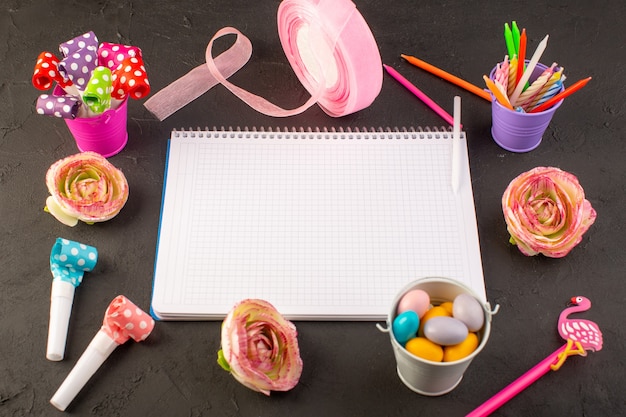 Ein Copybook und Bonbons der Draufsicht zusammen mit Blumenkerzen und -stiften auf dem dunklen Schreibtischfarbfoto-Dekorationsbonbon