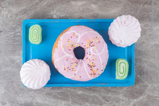 Ein Donut mit Geleebonbons und Keksen auf einer Platte auf Marmoroberfläche