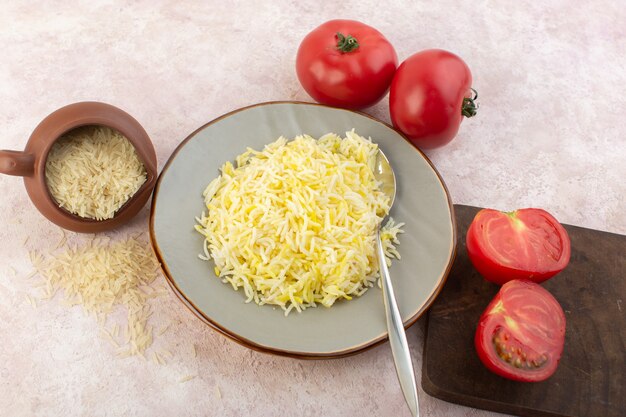 Ein Draufsicht gekochter Reis innerhalb Platte mit frischen roten Tomaten auf dem rosa Schreibtischlebensmittelmahlzeitgemüsegeschmack