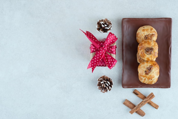 Kostenloses Foto ein dunkler teller mit keksen mit weihnachtsgeschenk und tannenzapfen.