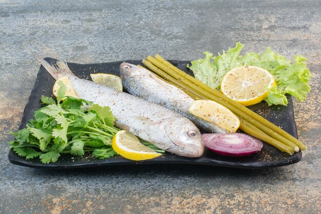 Ein dunkler Teller voller Fisch mit Zitrone und Grün auf Marmorhintergrund. Foto in hoher Qualität