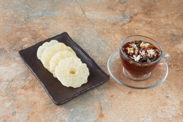 Ein dunkler Teller voller getrockneter gesunder Ananas und einer Tasse Tee