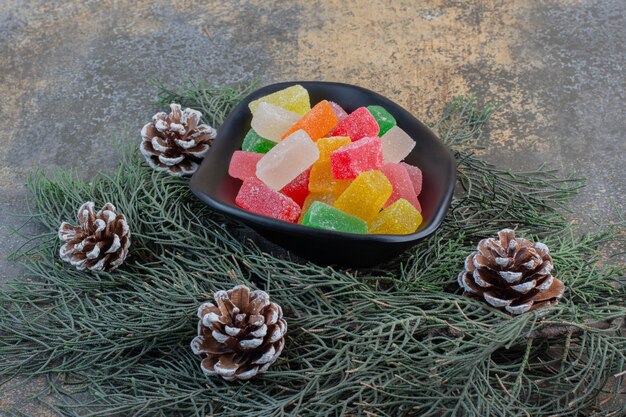 Ein dunkler Teller voller süßer Fruchtgelee-Bonbons und Tannenzapfen. Hochwertiges Foto