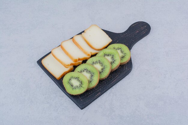 Ein dunkles Brett mit geschnittenem Brot und frischer Kiwi. Foto in hoher Qualität