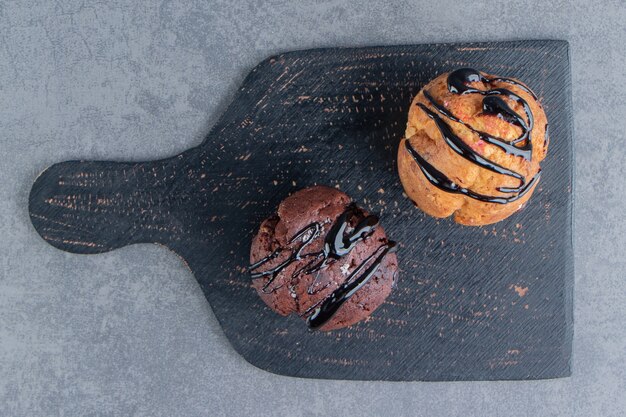 Ein dunkles Holzbrett mit zwei süßen Muffins