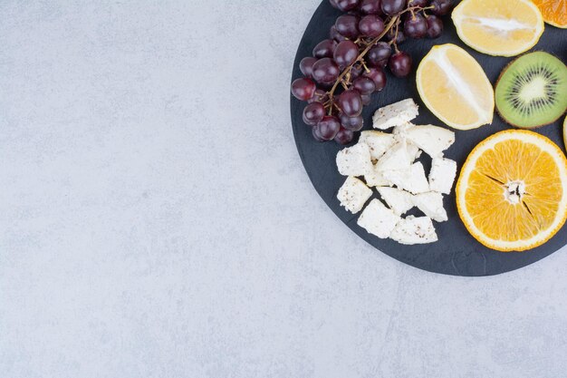 Ein dunkles Schneidebrett aus frischen süßen Früchten und geschnittenem Weißkäse. Foto in hoher Qualität