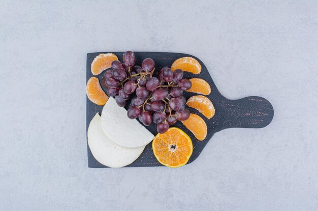 Ein dunkles Schneidebrett mit geschnittenem Käse und Früchten.