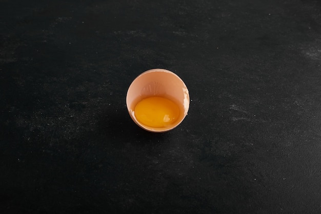 Ein Eigelb in der Eierschale auf schwarzer Oberfläche in der Mitte.