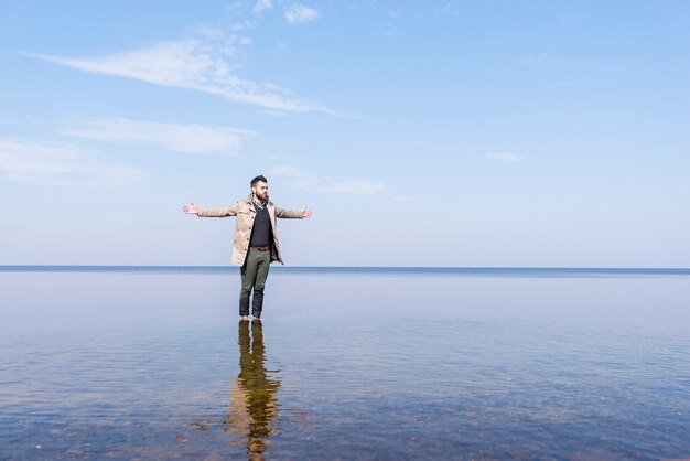 Ein einsamer junger Mann streckte die Hand aus und stand im seichten Meerwasser