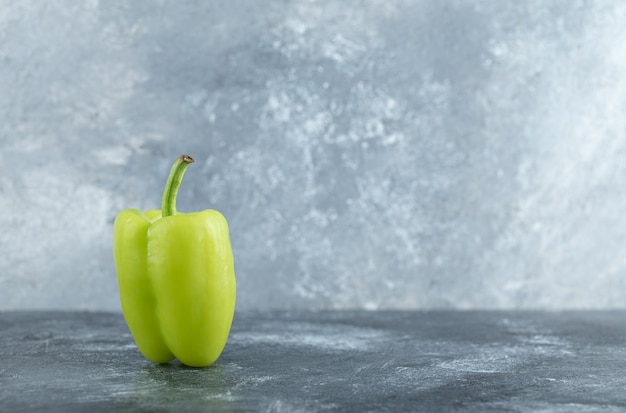 Ein einzelner grüner frischer Pfeffer auf grauem Hintergrund.