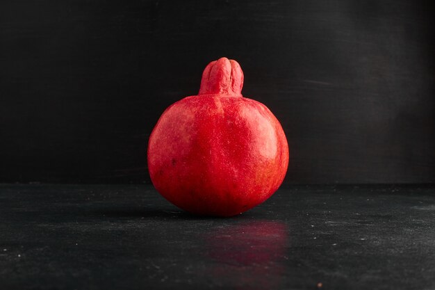 Ein einzelner roter Granatapfel auf schwarzem Raum.