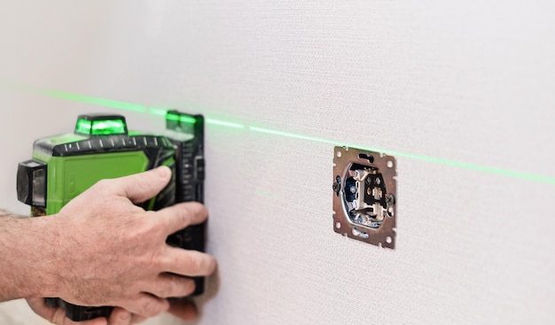 Ein Elektriker installiert Steckdosen in der Wohnung Überprüfung der installierten Steckdosen an der Wand der Wohnung mit einem selektiven Laserfokus auf die Steckdosen