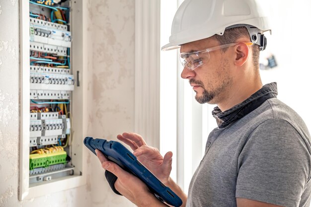 Ein Elektrotechniker, der in einer Schalttafel mit Sicherungen arbeitet, verwendet ein Tablet