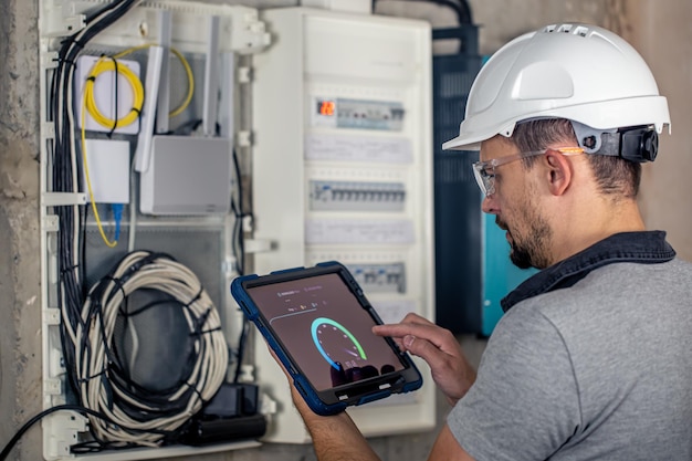 Kostenloses Foto ein elektrotechniker, der in einer schalttafel mit sicherungen arbeitet, verwendet ein tablet