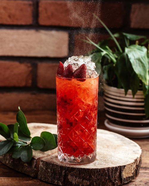 Ein Erdbeercocktail von vorne mit Eiswürfeln auf dem braunen Holztisch trinkt Jucie-Fruchtcocktail