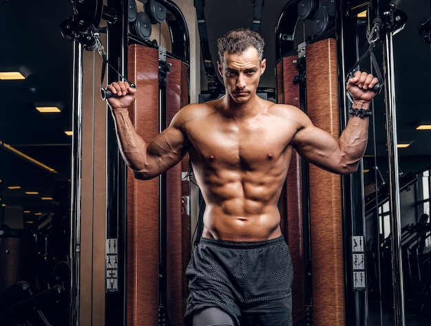 Ein ernsthafter attraktiver Mann macht Übungen mit Trainingsgeräten im dunklen Fitnessstudio.