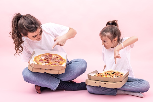 Ein erwachsenes Mädchen und ein kleines Mädchen mit verschiedenen Pizzen in Kartons, rosa Hintergrund.
