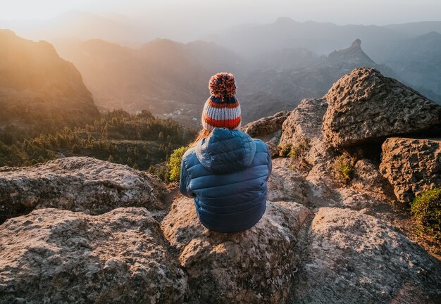 Ein faszinierender Blick auf felsige Berge von oben und eine Frau, die rückwärts sitzt