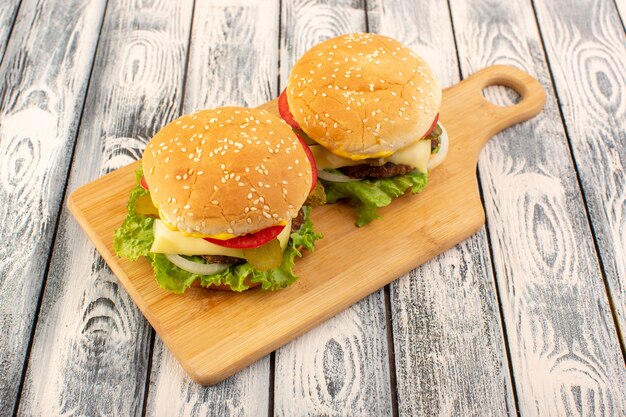 Ein Fleischburger von vorne mit Käse und grünem Salat auf dem Holztisch und dem grauen Tisch