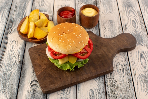 Ein Fleischburger von vorne mit Käse und grünen Salatkartoffeln und Dips auf dem Holztisch und grauem Tischessen