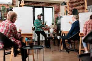 Kostenloses Foto ein freundlicher afroamerikanischer lehrer führt eine gruppe von menschen unterschiedlichen alters durch die grundlagen des zeichnens in der kunstklasse. ein junger lehrer erklärt den schülern während des workshops skizzentechniken