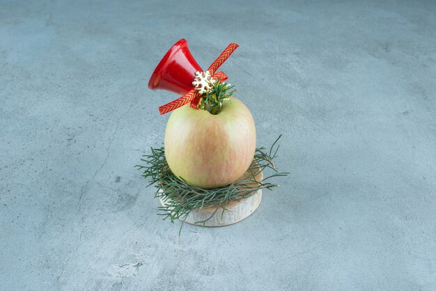 Ein frischer Apfel mit roter Weihnachtsglocke auf Marmor.