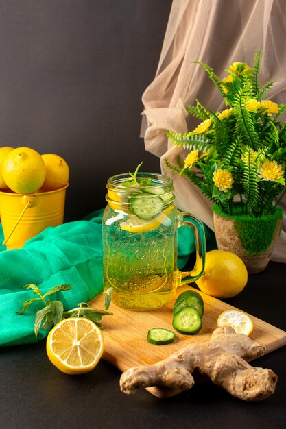 Ein frisches kühles Getränk des Zitronencocktails in der Vorderansicht in Scheiben geschnittene ganze Zitronen und ganze Zitronen zusammen mit Blumen auf dem dunklen Hintergrund Cocktailgetränkfrucht