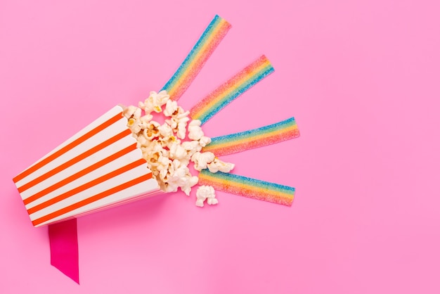 Ein frisches Popcorn der Draufsicht innerhalb des Papierpakets auf rosa Snack-Körnern der Filmfreunde