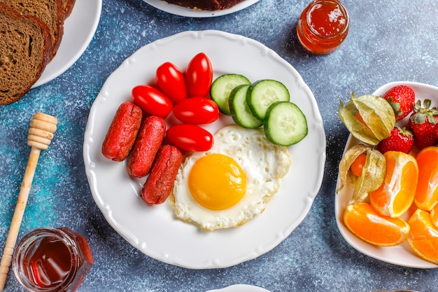 Ein Frühstücksteller mit Cocktailwürsten, Spiegeleiern, Kirschtomaten, Süßigkeiten, Früchten und einem Glas Pfirsichsaft.