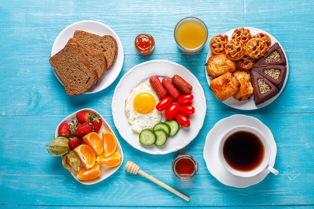 Ein Frühstücksteller mit Cocktailwürsten, Spiegeleiern, Kirschtomaten, Süßigkeiten, Früchten und einem Glas Pfirsichsaft.