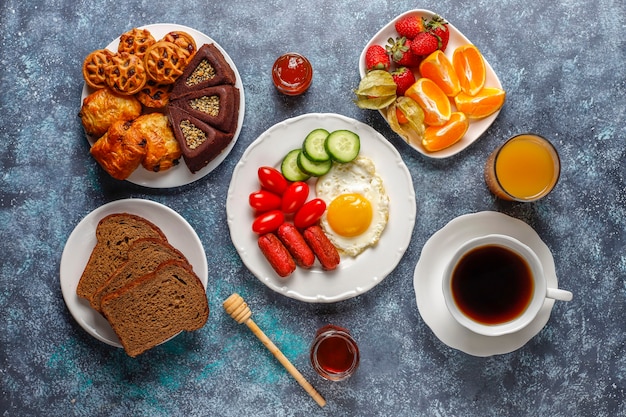 Ein Frühstücksteller mit Cocktailwürsten, Spiegeleiern, Kirschtomaten, Süßigkeiten, Früchten und einem Glas Pfirsichsaft.