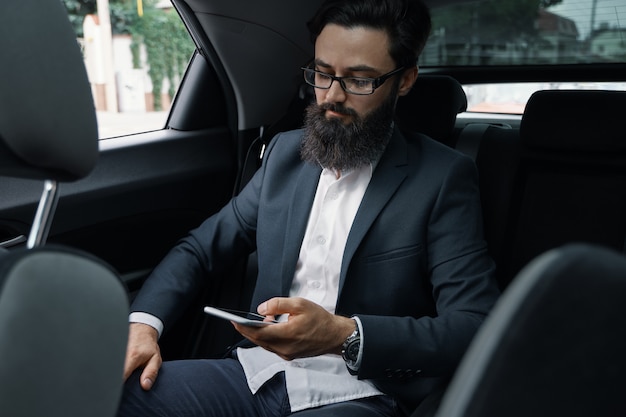 Ein Geschäftsmann während der Fahrt mit dem Auto auf dem Rücksitz unter Verwendung eines Smartphones