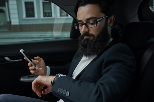 Ein Geschäftsmann während der Fahrt mit dem Auto auf dem Rücksitz unter Verwendung eines Smartphones