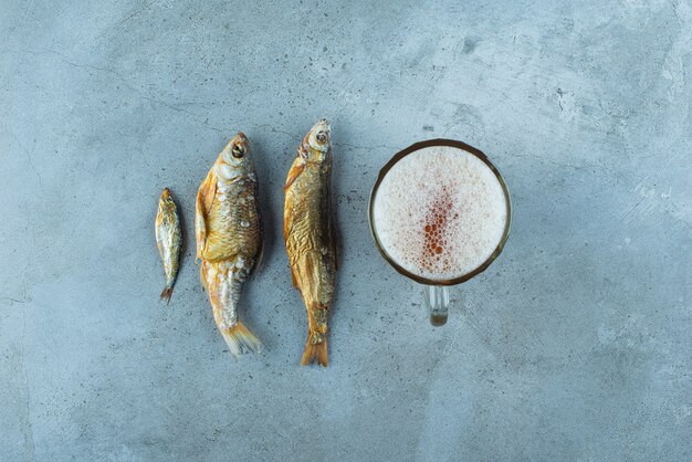 Ein Glas Bier neben Fischen auf dem blauen Tisch.