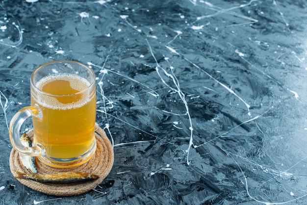 Ein Glas Bier und Fisch auf Untersetzer auf Blau.