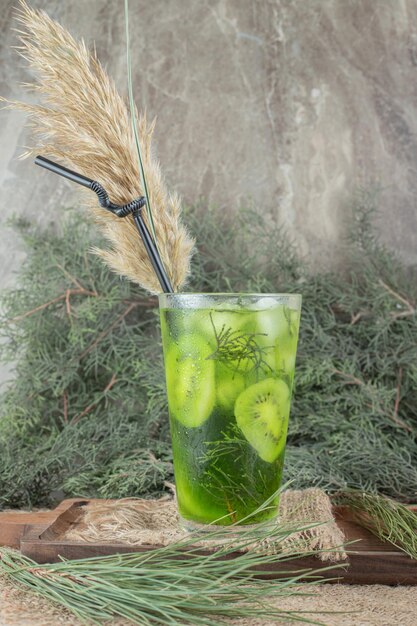 Ein Glas Fruchtsaft mit Kiwischeiben auf Holzteller.