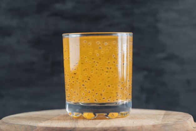 Ein Glas gelber Orangensaft auf schwarz auf einem Stück Holzbrett