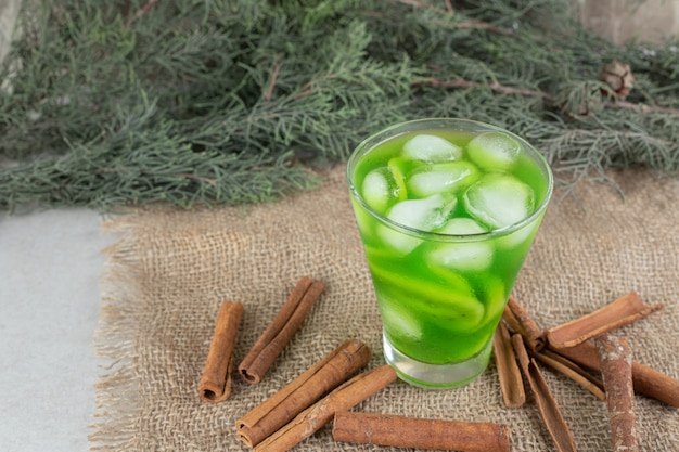 Ein glas kiwisaft und zimtstangen auf sackleinen