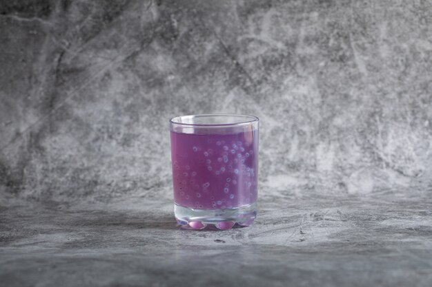 Ein Glas lila Blaubeersaft auf grau.