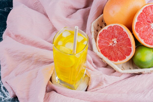 Ein Glas Limonade mit Zitronenscheiben und Grapefruits auf Marmoroberfläche.