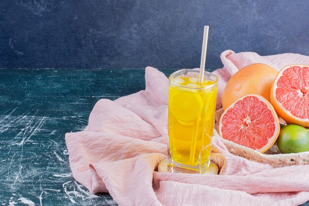 Ein Glas Limonade mit Zitronenscheiben und Grapefruits auf Marmoroberfläche.