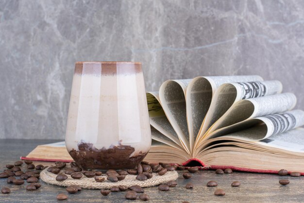 Ein Glas Milch mit geöffnetem Buch und Kaffeebohnen auf Marmorhintergrund. Foto in hoher Qualität